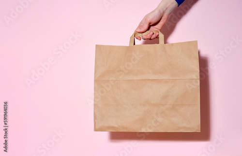 Female hand holding a paper bag with delivered items. Pink background