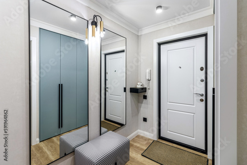 White entrance door in a modern renovated hallway with large mirrors and wardrobe