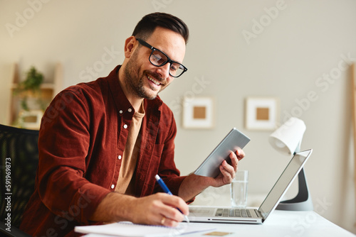 Young business man working at home with digital tablet and papers on desk.