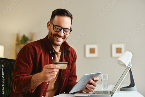 Young man holding credit card and tablet at home at table
