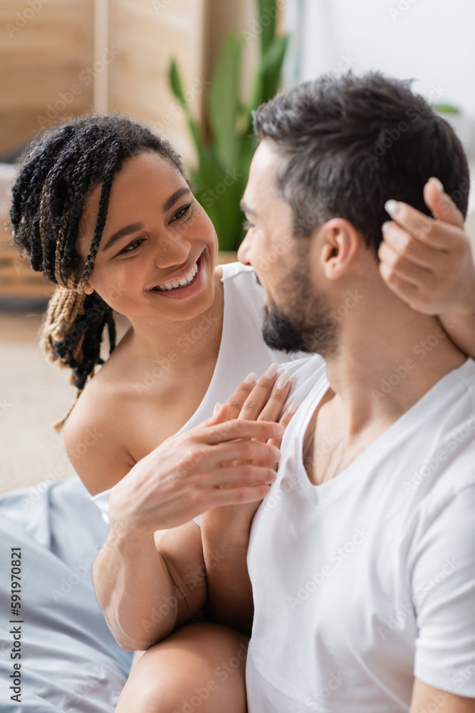 cheerful african american woman with dreadlocks looking at blurred boyfriend in bedroom at home. cheerful african american woman with dreadlocks looking at blurred boyfriend in bedroom at home.