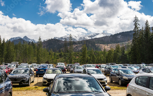 Crowded trails in the Tatra Mountains. Parking lot full of cars in the Kościeliska Valley. Early spring in the mountains. Snow-capped mountains in the background. Tatra Mountains, Poland