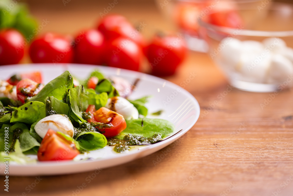 Plate of healthy classic close-up caprese salad with mozzarella cheese tomatoes and basil in kitchen - italian cuisine