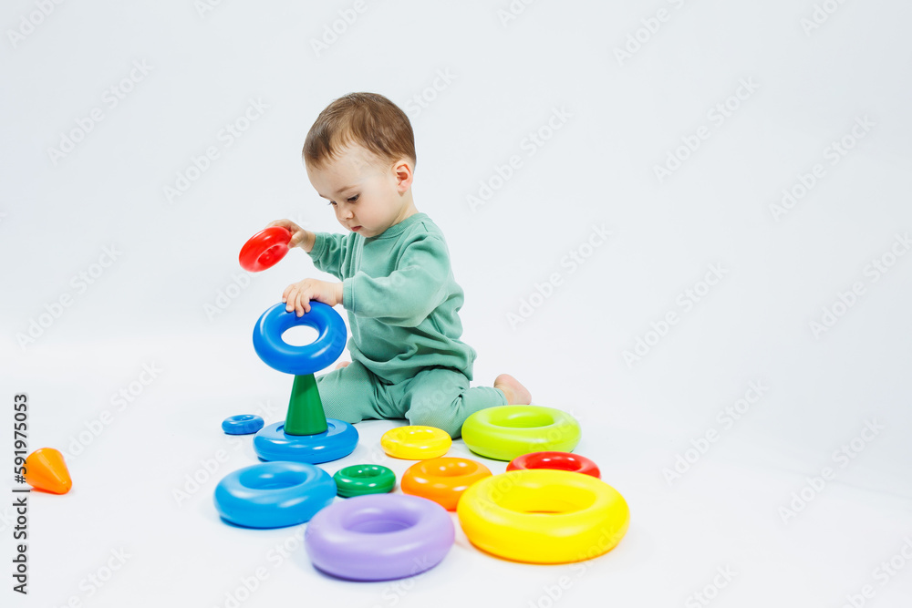 Cheerful little boy sitting with plastic educational toys on a white background. Child and toys for development. Development of children's motor skills. Cheerful little boy sitting with plastic educational toys on a white background. Child and toys for development. Development of children's motor skills.