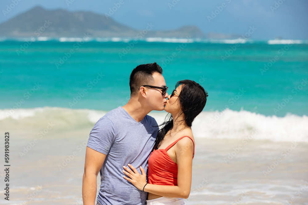 A couple shares a kiss while standing in the ocean surf while enjoying a tropical vacation along the coast of Oahu, Hawaii; Kailua, Oahu, Hawaii, United States of America A couple shares a kiss while standing in the ocean surf while enjoying a tropical vacation along the coast of Oahu, Hawaii; Kailua, Oahu, Hawaii, United States of America