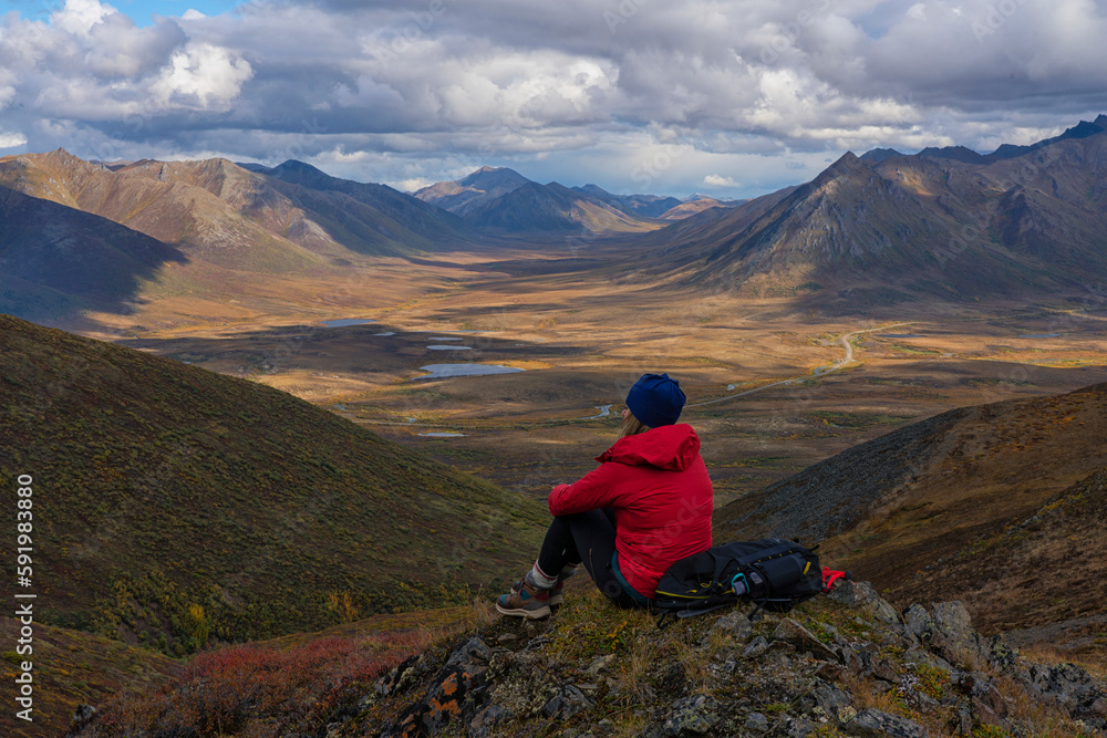 Woman sitting on a mountain above the Dempster Highway enjoying the scenery in Canada's Yukon; Yukon, Canada Woman sitting on a mountain above the Dempster Highway enjoying the scenery in Canada's Yukon; Yukon, Canada