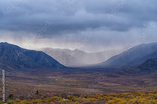 Rain clouds over mountains along the Dempster Highway create amazing landscapes while fall colors settle into the valley; Yukon, Canada photo