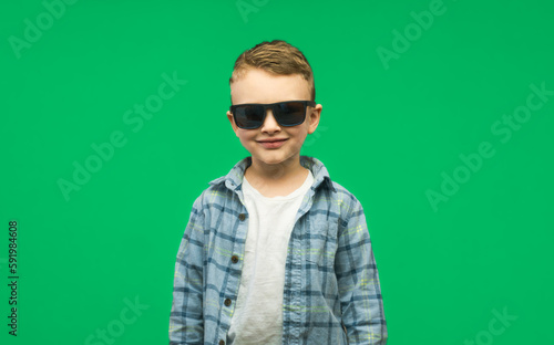 Photo of adorable young happy boy in sunglasses looking at camera. Isolated green background.