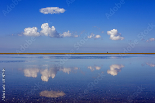 Fototapeta Naklejka Na Ścianę i Meble -  a smooth lake reflects clouds and a blue sky with a stretch of land in the middle