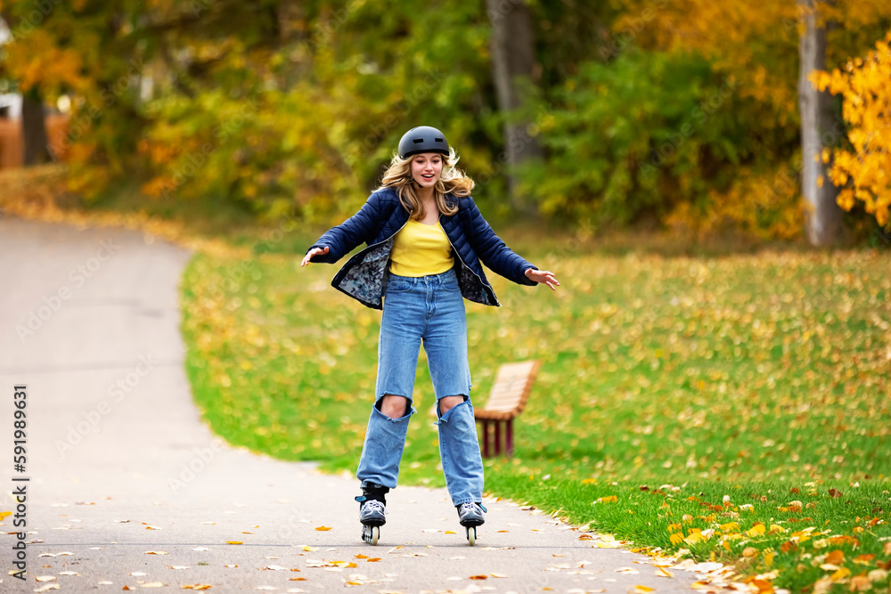 Teenage girl rollerblading down a walking path in a city park during a warm fall afternoon; St. Albert, Alberta, Canada Teenage girl rollerblading down a walking path in a city park during a warm fall afternoon; St. Albert, Alberta, Canada