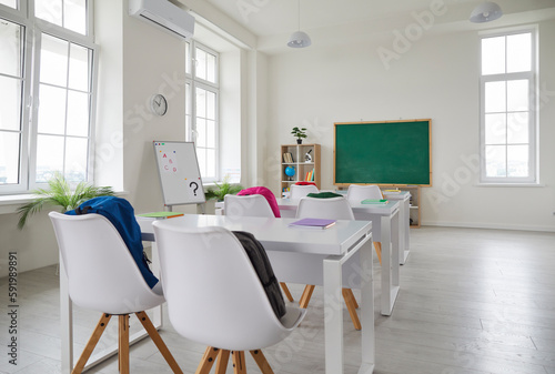 School classroom. Interior of spacious classroom at new modern school. Back to school. Clean empty room with white walls  big windows  comfortable desks  chairs  green chalkboard  whiteboard