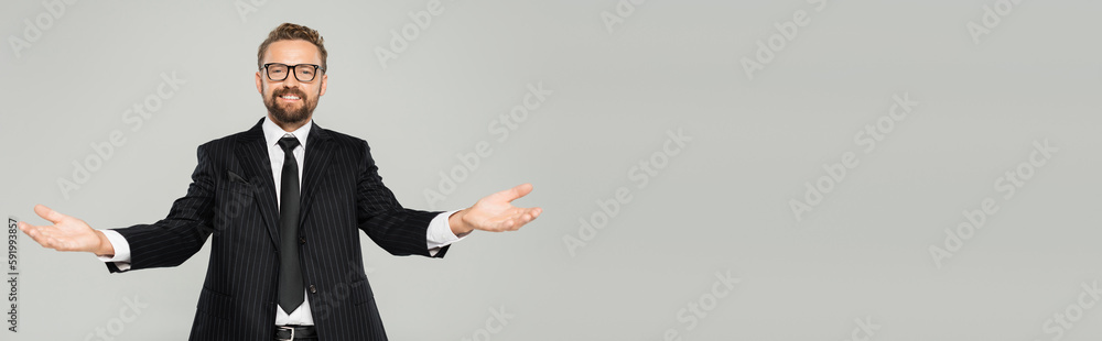 happy businessman in suit and glasses looking at camera and showing welcoming gesture isolated on grey, banner. happy businessman in suit and glasses looking at camera and showing welcoming gesture isolated on grey, banner.