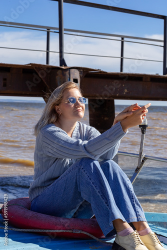 Portrait of a young beautiful girl in a blue sweater and jeans is on a boat near the river pier.