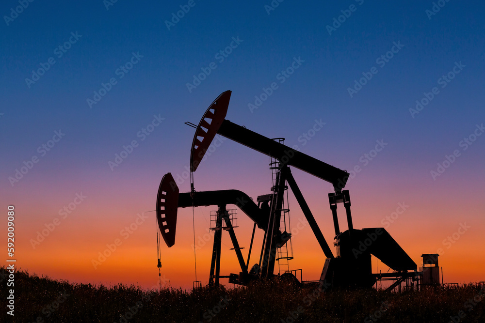 Silhouette of two pumpjacks at sunrise with glowing sky in the background, West of Airdrie; Alberta, Canada Silhouette of two pumpjacks at sunrise with glowing sky in the background, West of Airdrie; Alberta, Canada