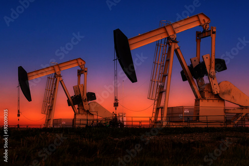 Glowing colourful pumpjacks at sunrise with glowing sky in the background, West of Airdrie; Alberta, Canada photo