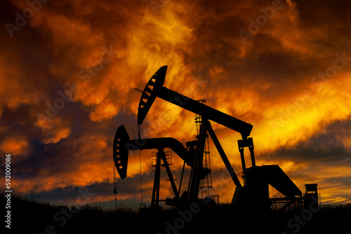 Silhouette of two pumpjacks at sunrise with dramatic colourful glowing clouds in the background, West of Airdrie; Alberta, Canada photo