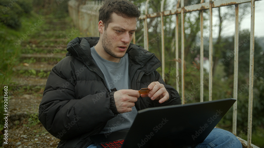 Fototapeta premium Handsome Man outside checking his credit card on the laptop went mad when he realized he had been scammed