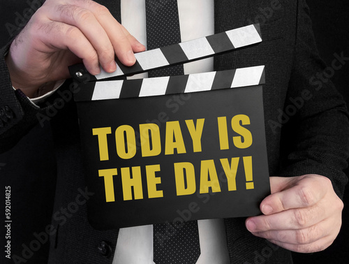 A businessman holds up a ?lapperboard with text Today Is The Day! photo