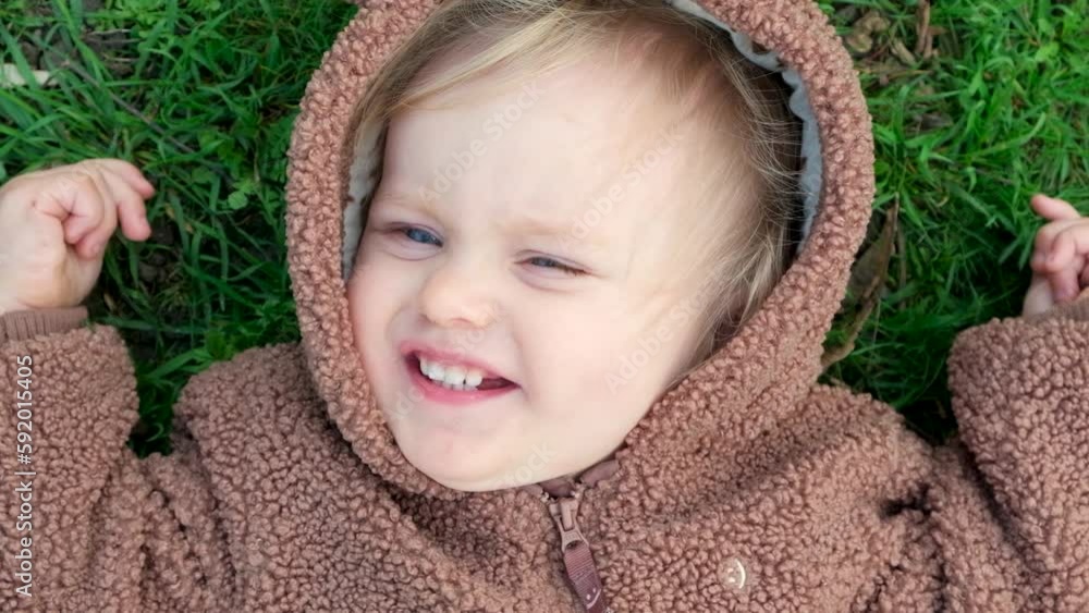 Portrait of a one-and-a-half-year-old blue-eyed girl in a bear costume lying on the grass, view from above Portrait of a one-and-a-half-year-old blue-eyed girl in a bear costume lying on the grass, view from above