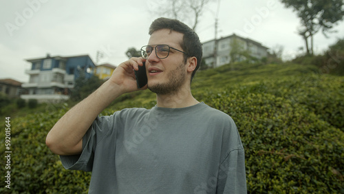 Helpful and Happy: Young, Handsome, Glasses-Wearing Man Calls Customer Support on His Cell Phone Outdoors