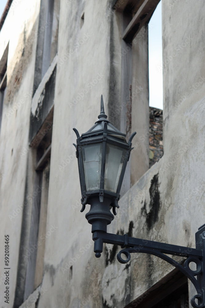 Old Black Metal Street Lamp on a Gray Concrete Wall next to an Open Window