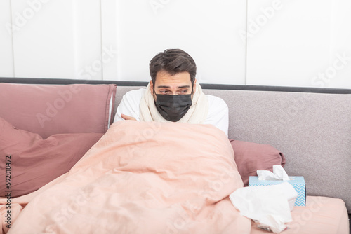 Sick man lying in the bed, suffering from high fever and flu. He tries to treat himself at home 
