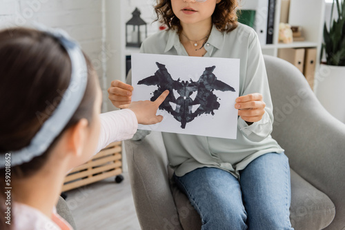 Blurred girl pointing at Rorschach test near psychologist in consulting room. photo