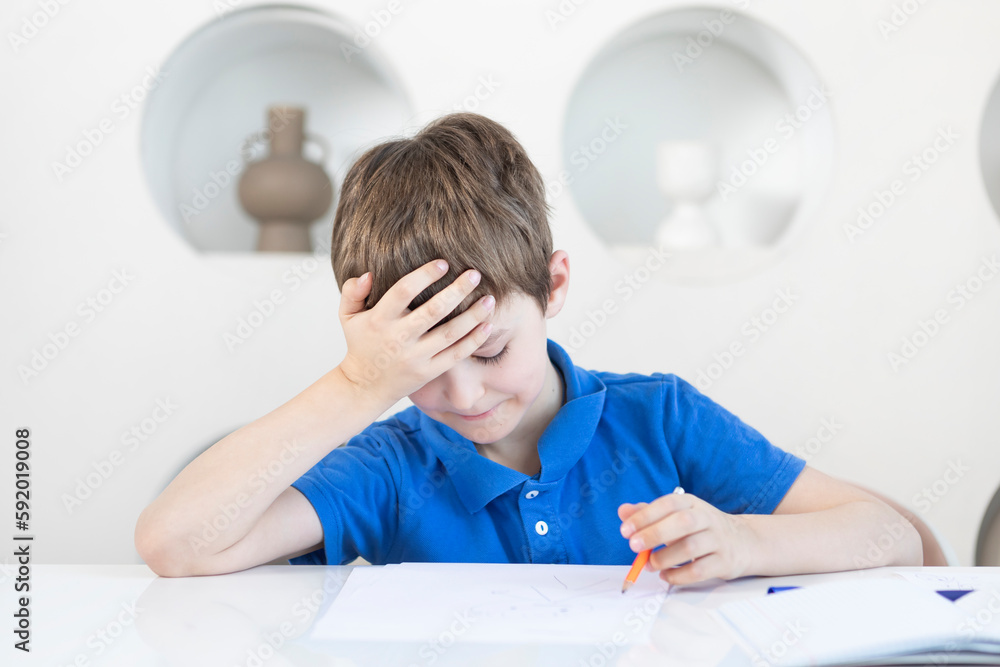 Tired and bored school boy sits at the desk and tries to study Tired and bored school boy sits at the desk and tries to study