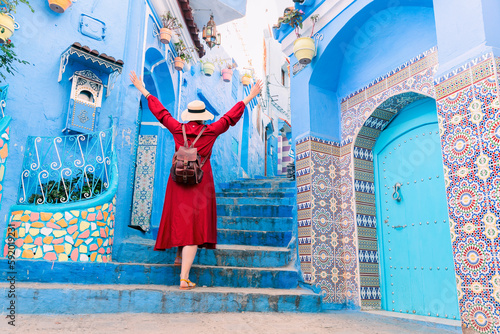 Colorful journey from Morocco. young tourist in red dress walking in the medina of the blue city Chefchaouen.
