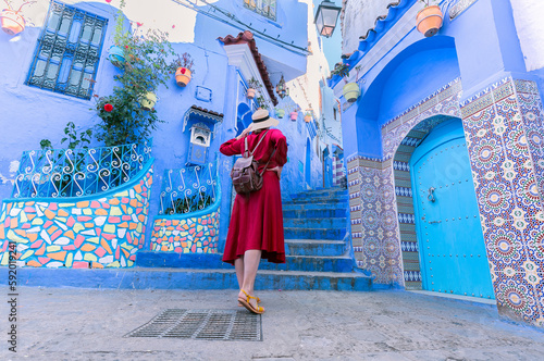 Colorful journey from Morocco. young tourist in red dress walking in the medina of the blue city Chefchaouen. © minoandriani