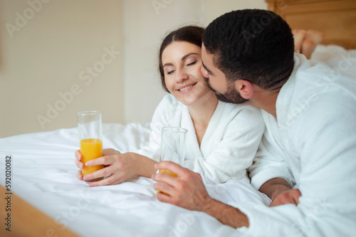 Man Kissing Woman Lying In Bed In Hotel Room Indoor