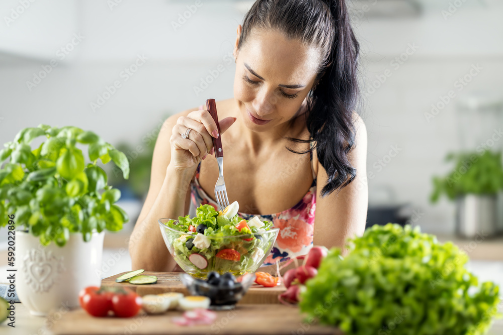 Healthy lifestyle young woman eating lettuce salad. Young brunette eating healthy food in her kitchen