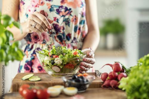 A young woman tastes a healthy salad with a fork in her kitchen