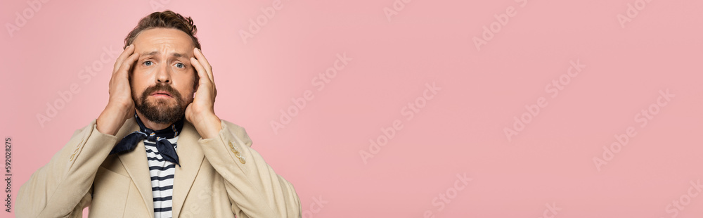 tensed man in blazer and neck scarf looking at camera while holding head isolated on pink, banner. tensed man in blazer and neck scarf looking at camera while holding head isolated on pink, banner.