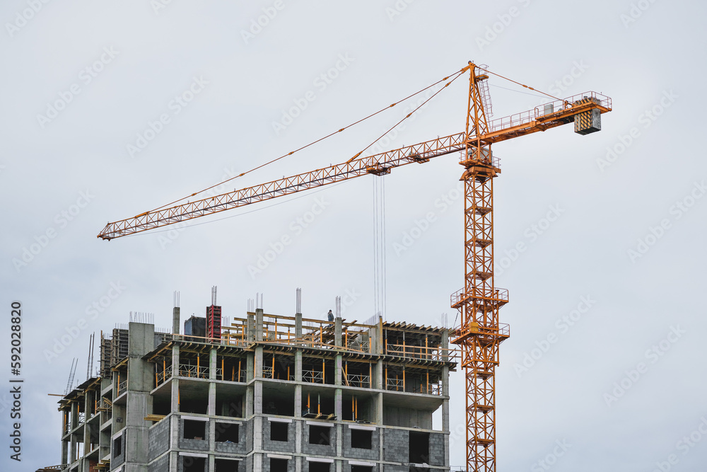 High building yellow crane working on construction site near unfinished house at urban street outdoor. Development and real estate concept. High building yellow crane working on construction site near unfinished house at urban street outdoor. Development and real estate concept.