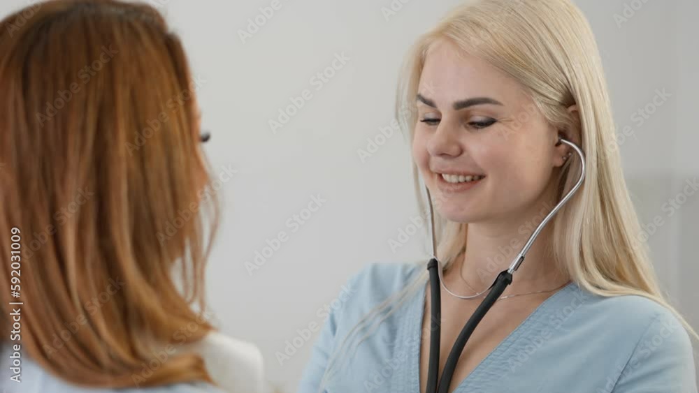 A young woman at a medical examination. A female doctor listens to a patient with a stethoscope. Diagnosis in a health care clinic. Hospital admission, treatment of heart and lung diseases. A young woman at a medical examination. A female doctor listens to a patient with a stethoscope. Diagnosis in a health care clinic. Hospital admission, treatment of heart and lung diseases.