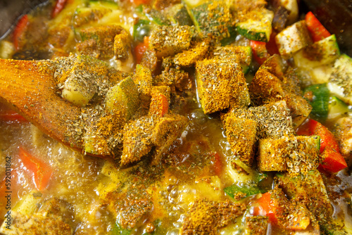 Frying pan with stewed vegetables in sauce and spices with a wooden spoon close-up.