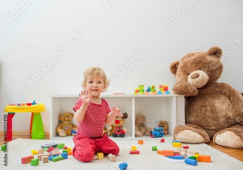 Sweet happy child boy having fun at home playing with his giant teddy bear and colorful wooden blocks and toys, on the floor.