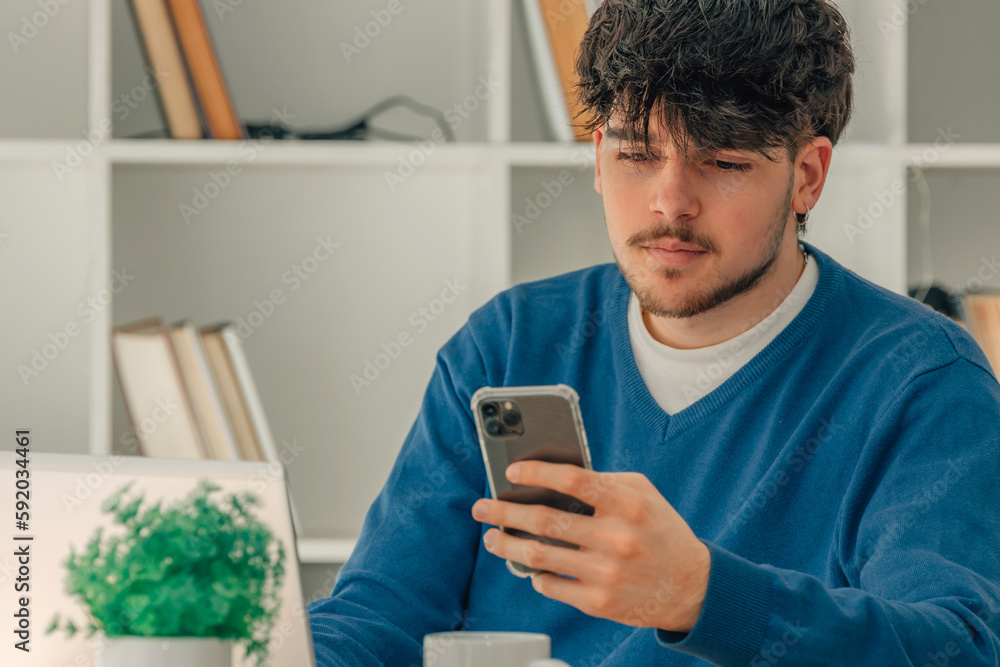 young male student with mobile phone and laptop at desk young male student with mobile phone and laptop at desk