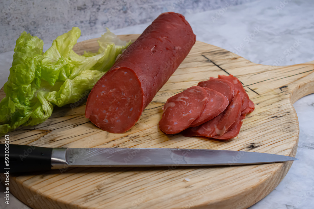Vegan salami sausage made with washed flour and bits og vegan cheese fat, sliced on wooden board Vegan salami sausage made with washed flour and bits og vegan cheese fat, sliced on wooden board