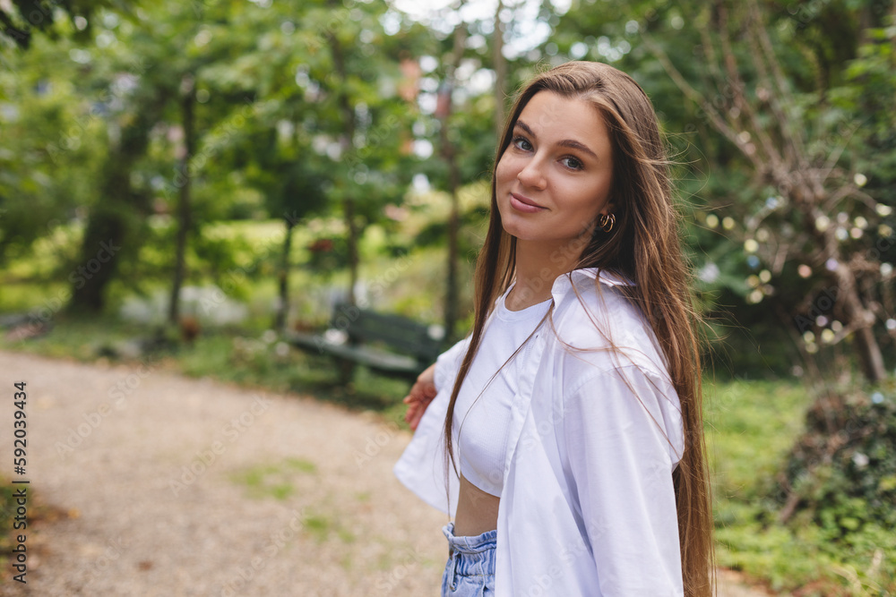 Attractive brunette woman walk on the countryside street. Girl wear white shirt and top and look happy and smiles. Woman walk on the street, she turn around and look joy, flying long hair. Side view.