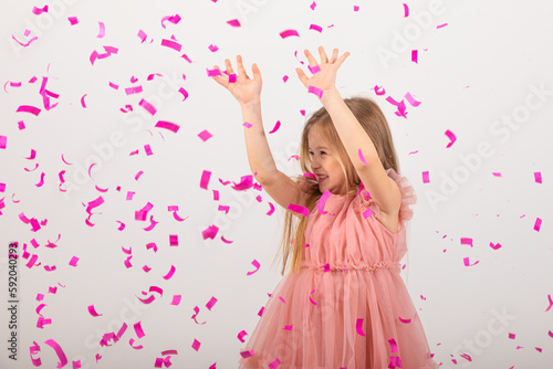 little girl blonde in a pink dress catches confeti smiling happy on white background, holiday concept. A child is celebrating a birthday on a white background