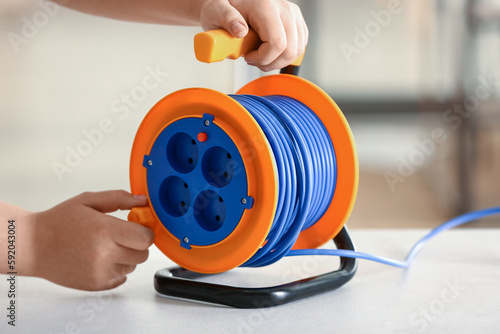 Female hands with extension electric cable reel on table, closeup