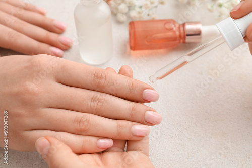 Tela Manicure master applying cuticle oil onto female fingernails on light background