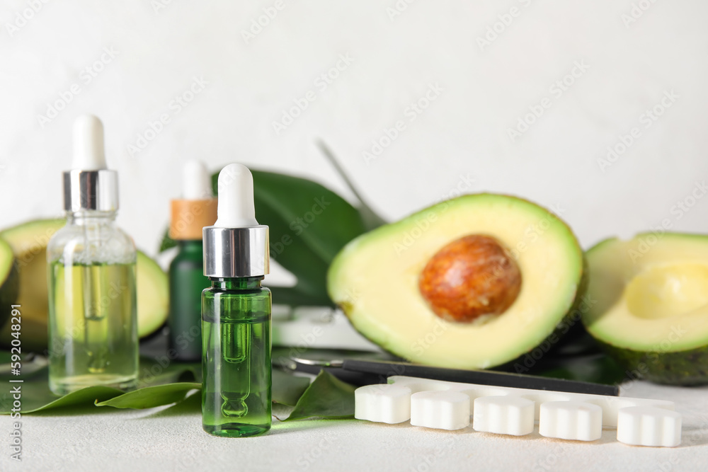 Composition with bottles of cuticle oil, manicure instruments, avocado and palm leaf on light background, closeup