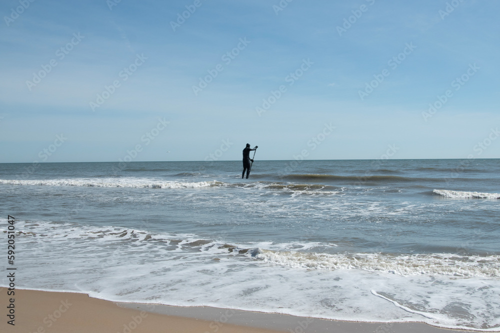 A person in a wetsuit, Standing up and paddle boarding in the Atlantic Ocean, VA. Beach USA. 