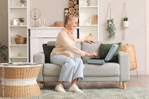 Mature woman with record player sitting on sofa at home