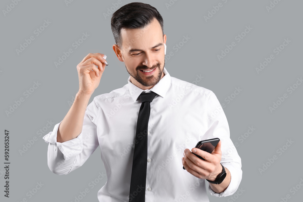 Handsome businessman in earphones using mobile phone on grey background Handsome businessman in earphones using mobile phone on grey background