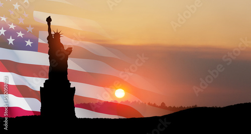 Statue of Liberty with a large american flag and sunset sky on background. © hamara