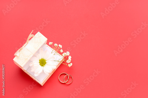 Box with flowers and wedding rings on red background © Pixel-Shot